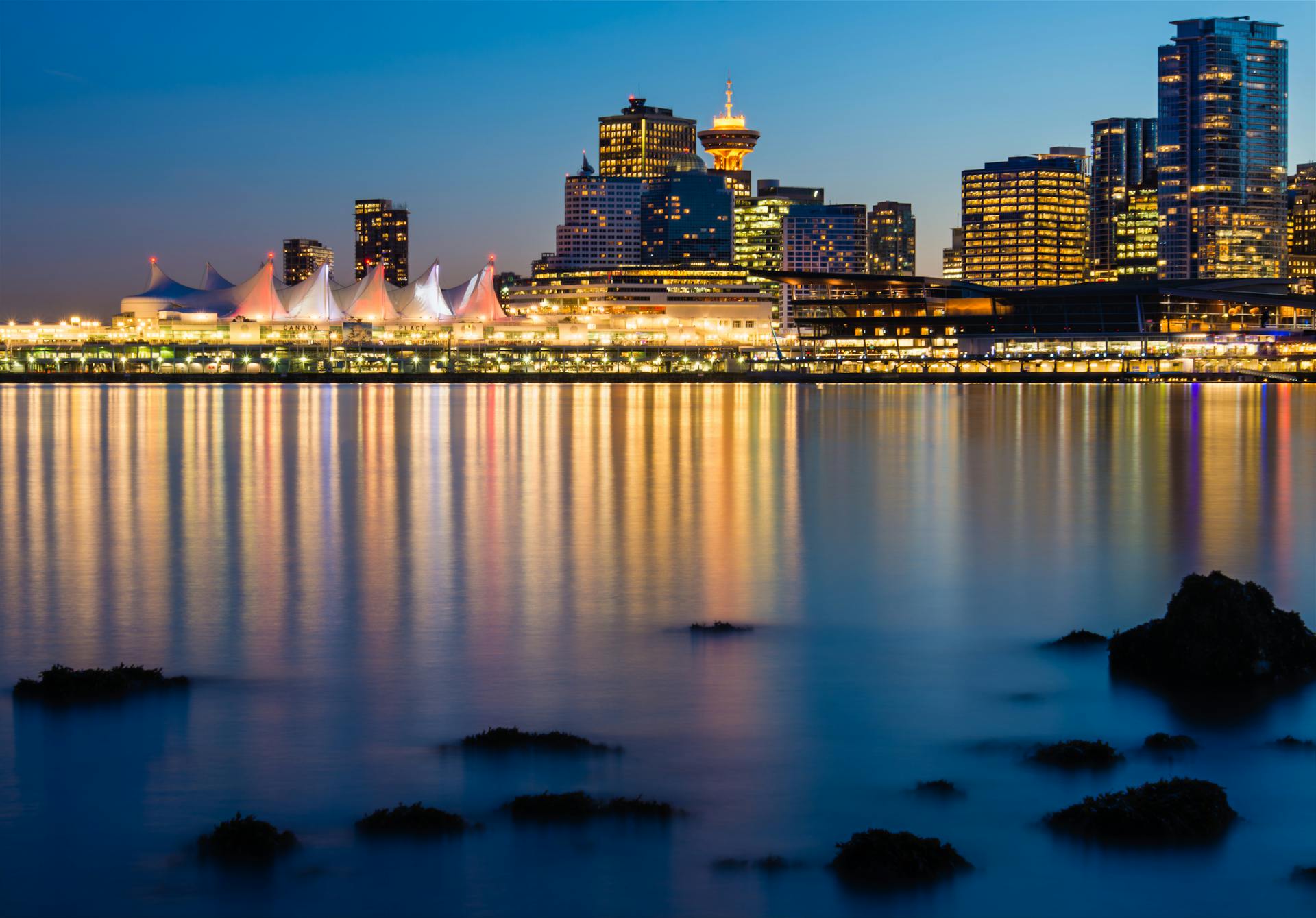 Vancouver harbour at dusk — Canada Place sails, Harbour Centre lookout tower, and downtown highrises reflected in Burrard Inlet