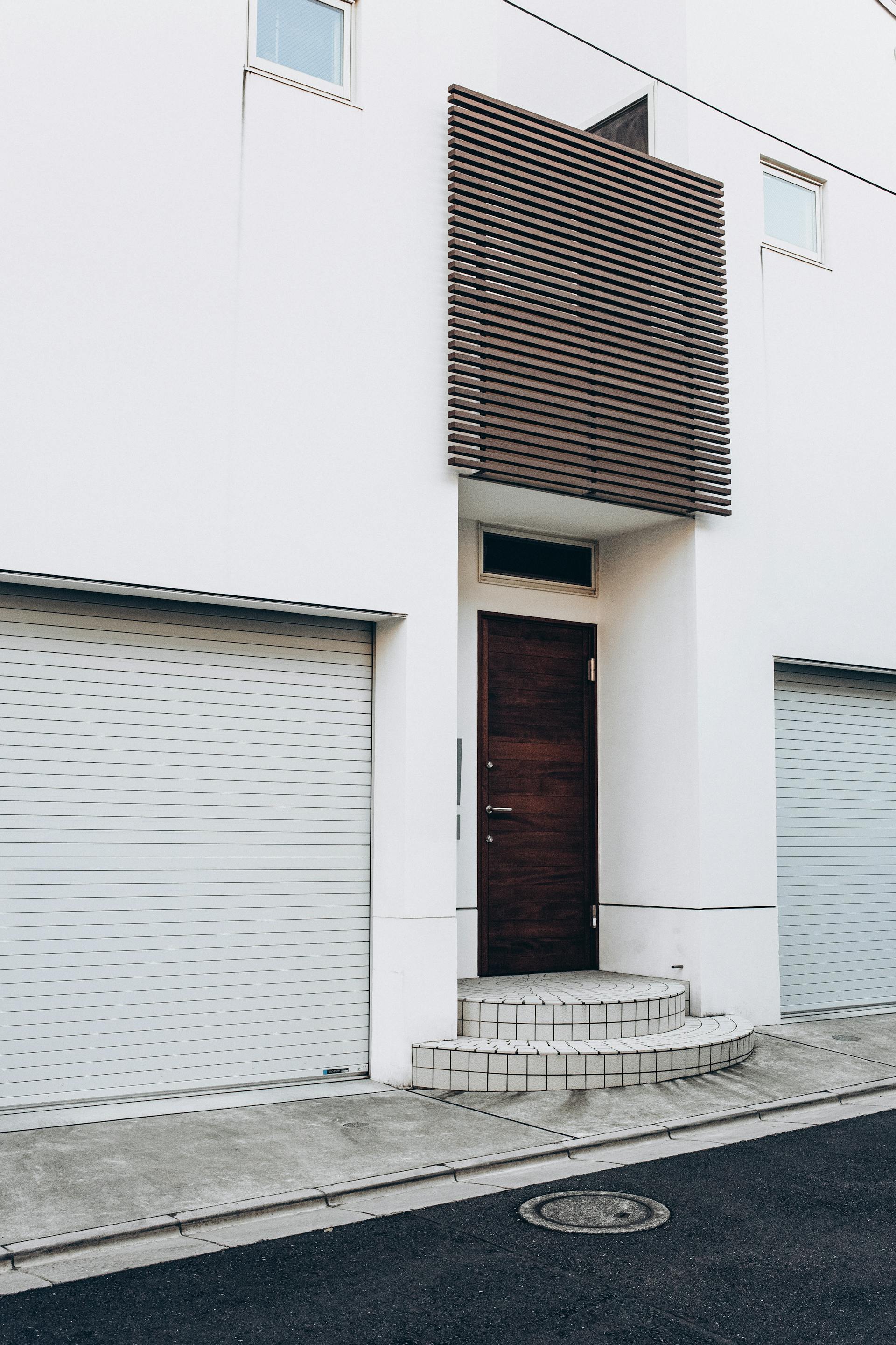 A minimalist two-unit white duplex with a wooden front door and twin garage entrances on a quiet residential street
