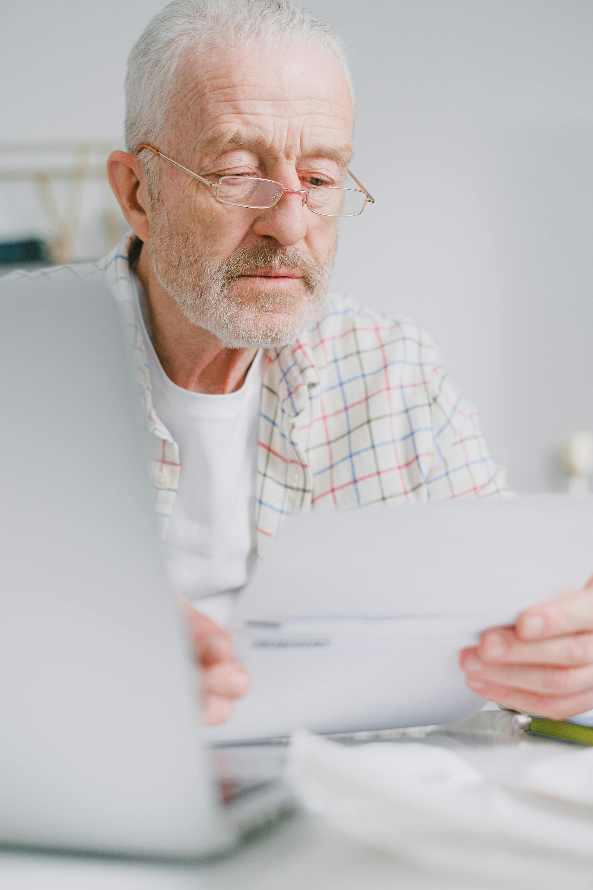 A council chair concentrates on paperwork at a home desk in warm natural light, glasses pushed up, working through strata correspondence